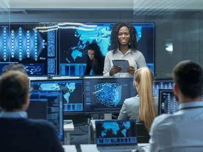 Several people in a technology room with multiple monitors with technical graphics